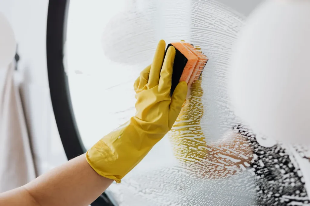 Gloved hand scrubbing a bathroom mirror