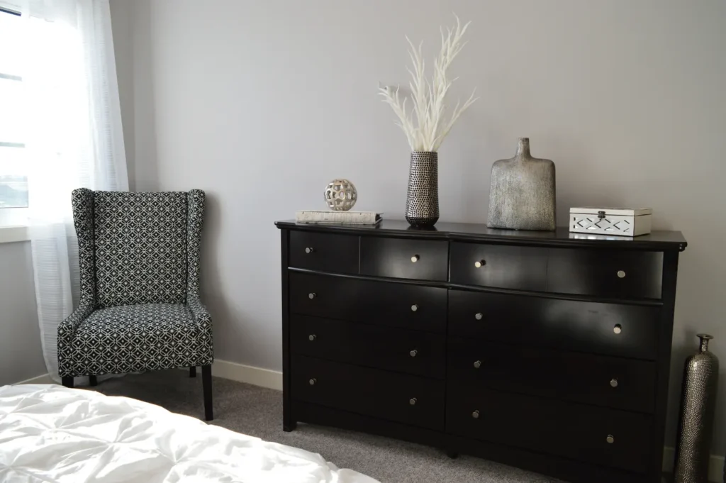 Black dresser in a bedroom beside an armchair