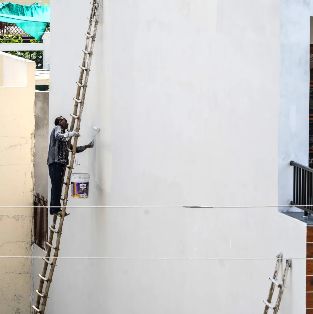 Painter on a ladder painting a tall white wall