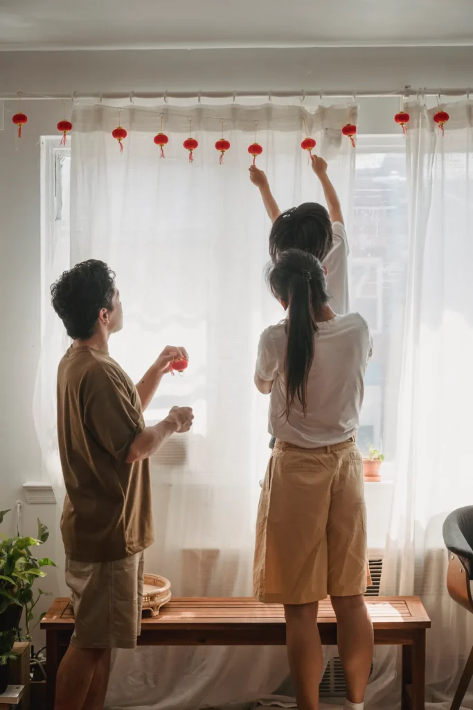 Two women hanging curtains at a bright window