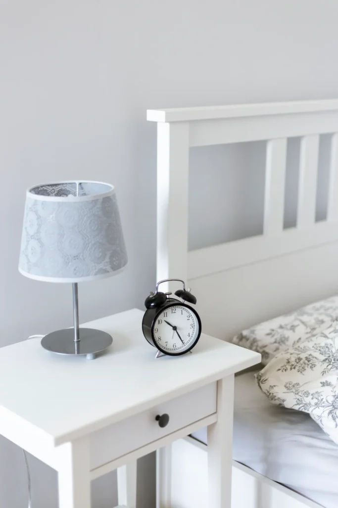 White nightstand with a lamp and alarm clock