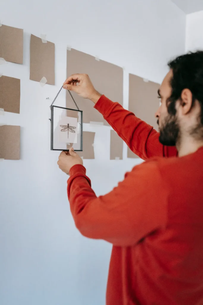 Man hanging a glass picture frame on a wall