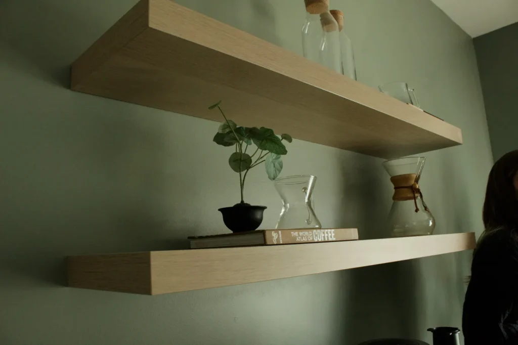 Two floating wood shelves on a sage-green wall
