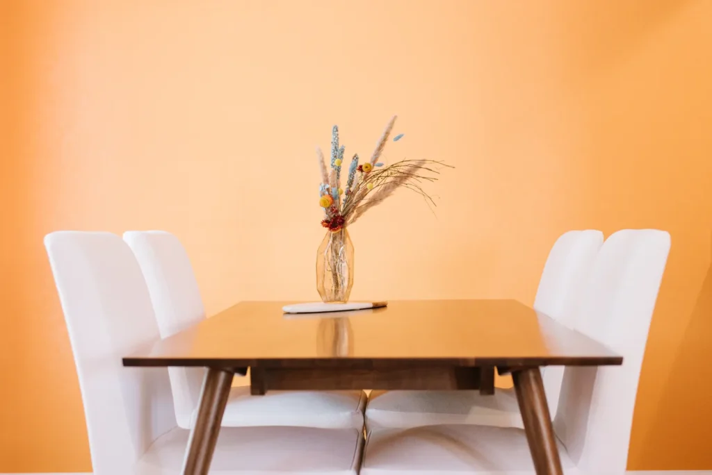 Dining table with white chairs against an orange wall